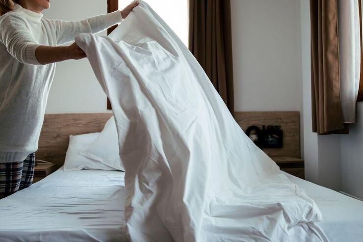 Donna rifà il letto sistemando lenzuola bianche