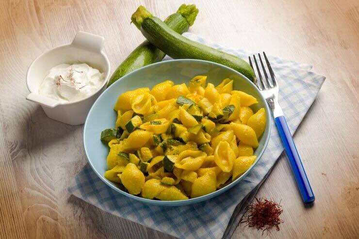 Piatto di pasta con zucchine. A lato una crema bianca e zafferano