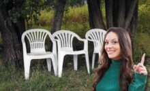 Ragazza con dito in su, sorridente e dietro di lei tre sedie di plastica bianche nel verde