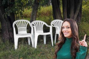Ragazza con dito in su, sorridente e dietro di lei tre sedie di plastica bianche nel verde