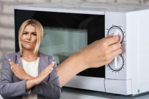 Ragazza in primo piano fa X con le braccia, sul forno mano gira manopola del microonde