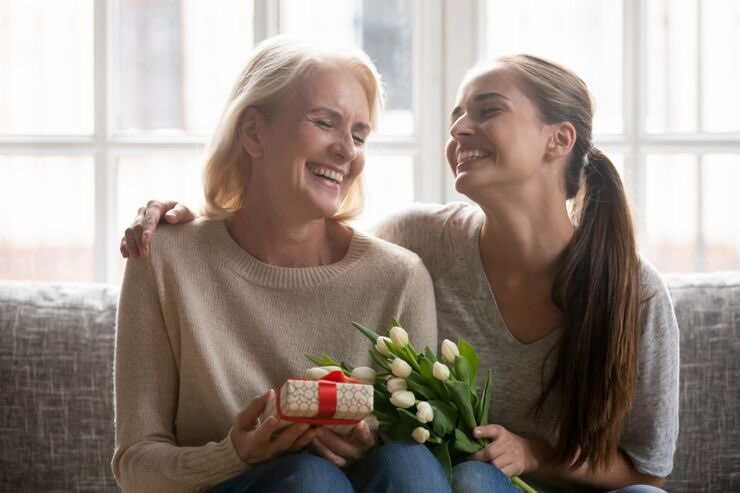 Donna e figlia sorridenti con pacco regalo e fiori in mano