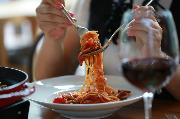 persona che mangia una pasta al pomodoro e beve un bicchiere di vino