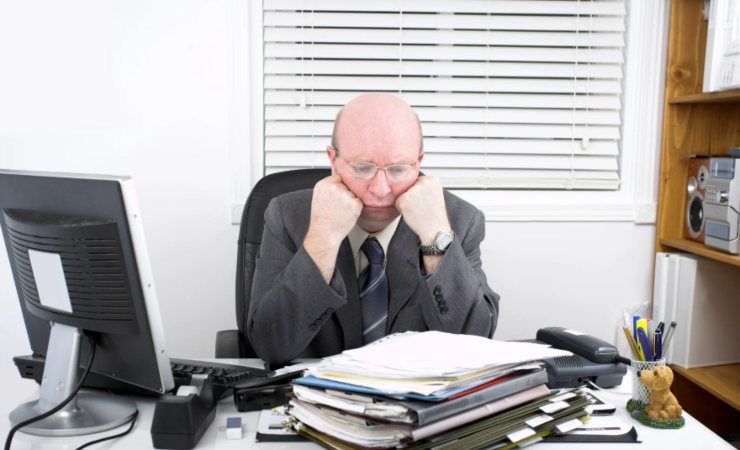 uomo triste seduto alla scrivania con davanti fogli e cartelle da lavoro