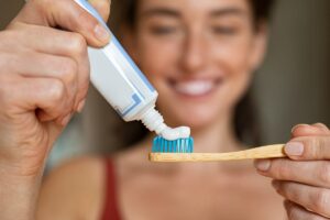 donna in sfondo che mette il dentifricio su uno spazzolino